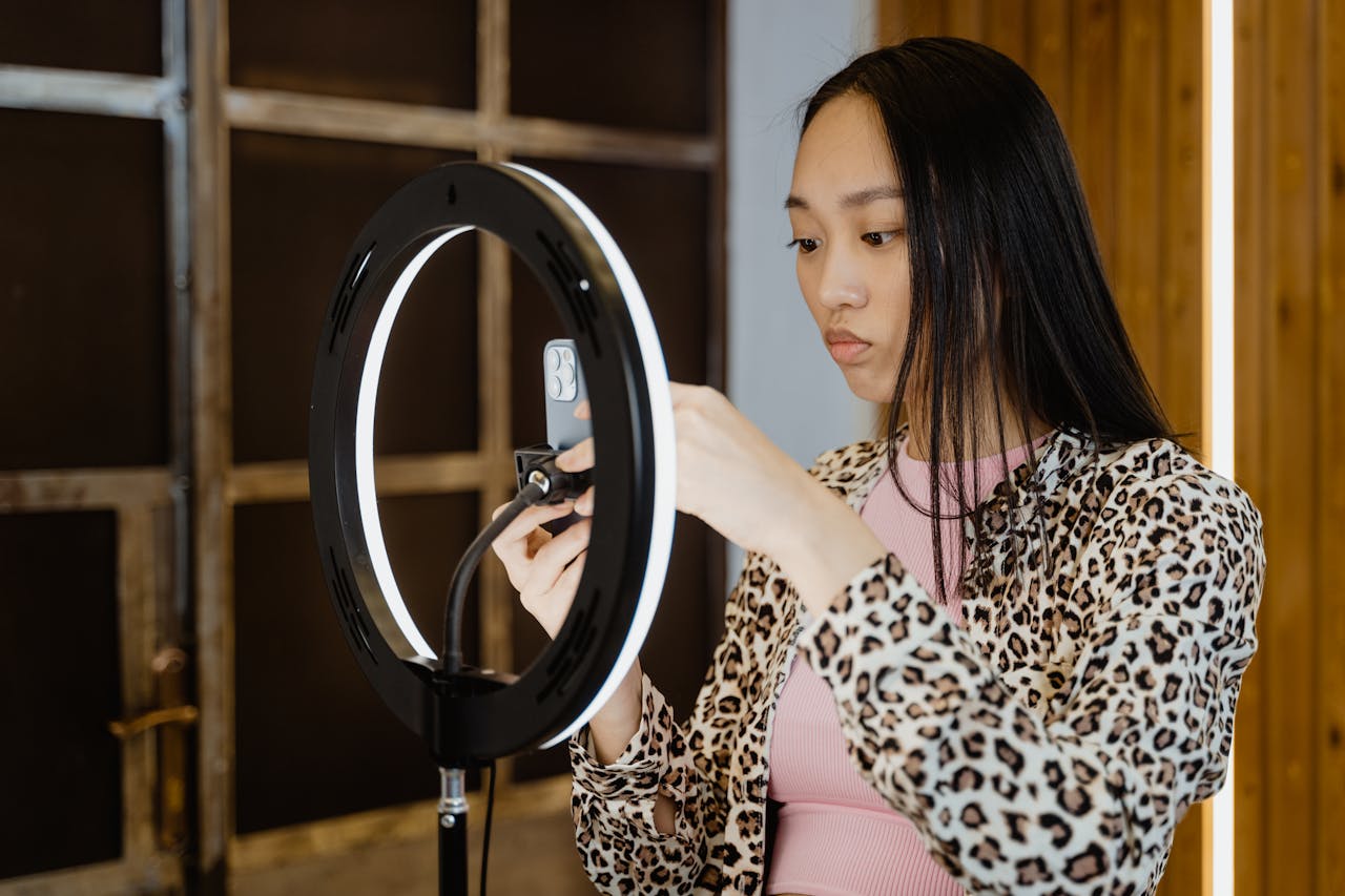 Asian woman with leopard print jacket adjusts ring light for smartphone streaming setup.